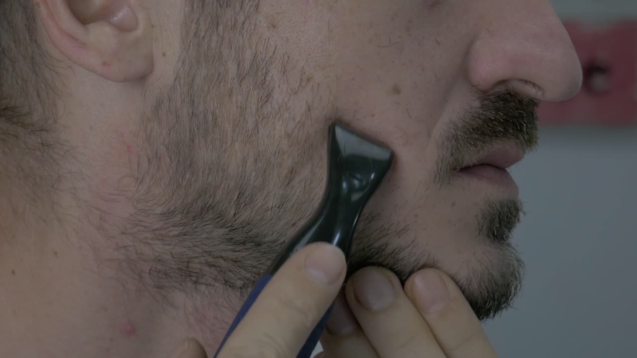 hombre caucásico afeitando su barba de mejilla con una maquinilla de afeitar de batería para dar forma al contorno