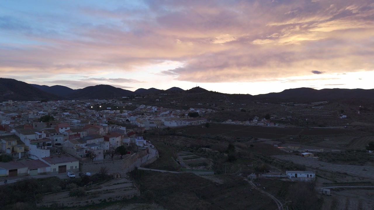 Timelapse statico con drone che mostra la campagna di Bullas al tramonto, con nuvole in movimento, campi coltivati e sagome di montagne lontane.