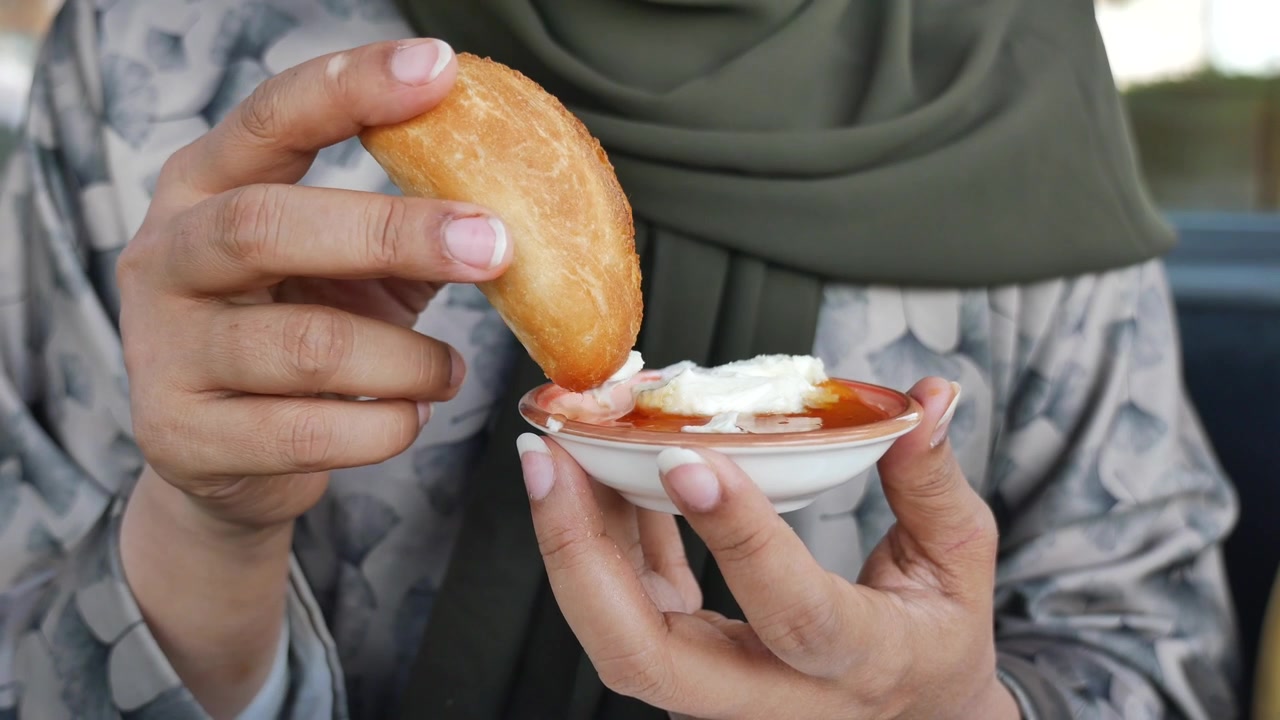 Woman Dipping Fried Pastry into Cream and Syrup