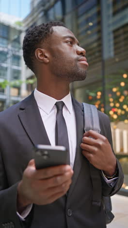 Vertical-Video-Shot-Of-Young-Businessman-Wearing-Suit-Using-Mobile-Phone-Standing-Outside-Offices-In-The-Financial-District-Of-The-City-Of-London-UK-Shot-In-Real-Time