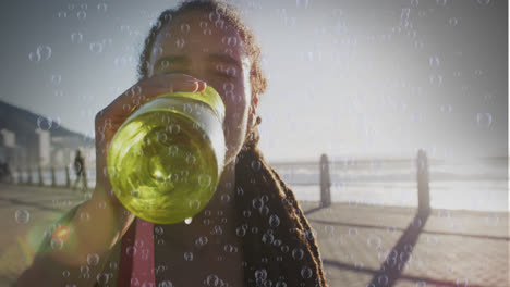 Animación-De-Burbujas-Sobre-Mujer-Birracial-Bebiendo-Agua-En-El-Paseo-Marítimo