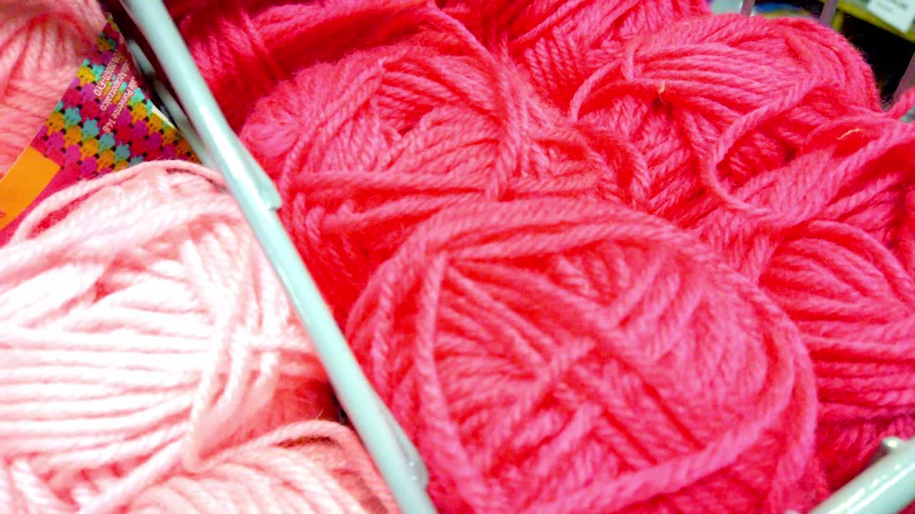 Soft pink and red yarn balls displayed in a store basket under natural lighting