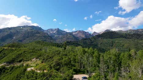 Pull-back-aerial-view-of-a-mountain-road-with-a-truck-parked-along-the-trail-and-rugged-mountains-in-the-distance