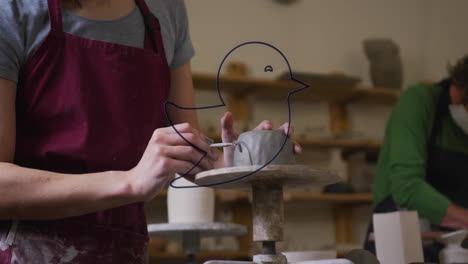 Person shaping clay with blue bird outline animation over pottery studio scene