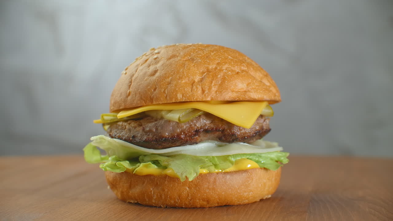 gran hamburguesa con carne de res, chuleta, tomates, setas y pepinos con queso derretido gira en una tabla de madera sobre un fondo claro.