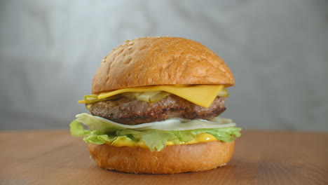 gran hamburguesa con carne de res, chuleta, tomates, setas y pepinos con queso derretido gira en una tabla de madera sobre un fondo claro.