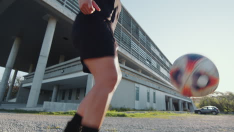 female athlete practicing kick-ups with soccer ball on street