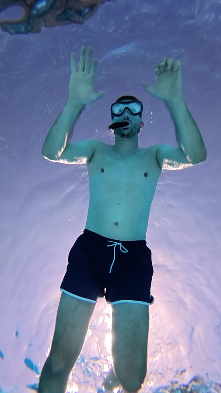 Vista subacquea di un uomo con maschera da snorkeling che nuota in piscina, ripreso in ultra slow motion cinematografico per una scena acquatica drammatica