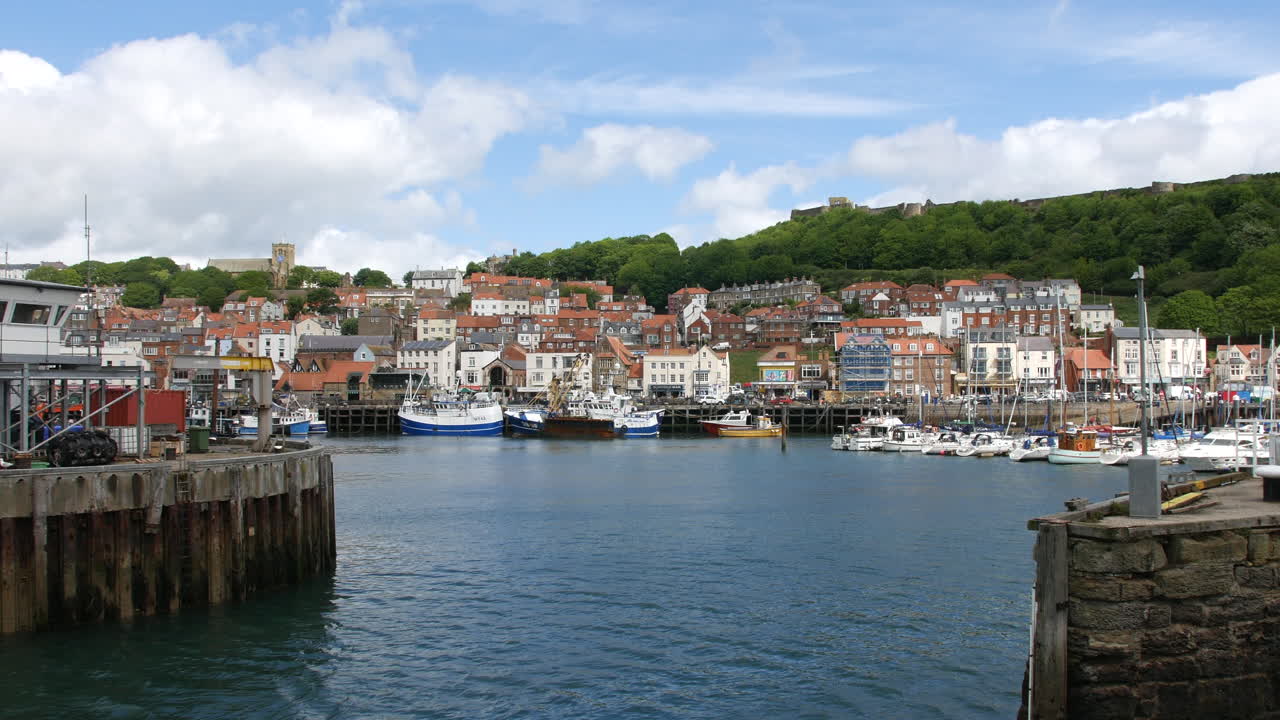 A harbor view in Scarborough, North Yorkshire in England showing fishing boats and yachts docked near the waterfront with hillside homes and castle ruins