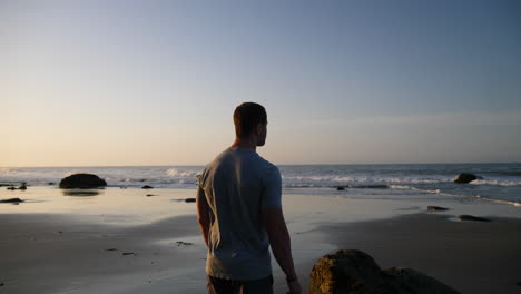 un hombre fuerte mirando las olas del océano y estirándose para correr y hacer ejercicio en la playa al amanecer en santa barbara, california a cámara lenta