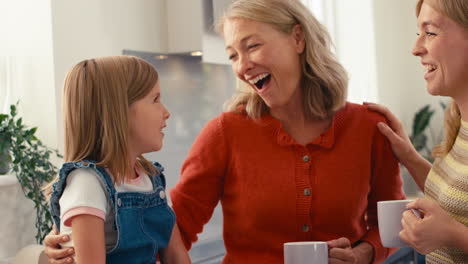 Familia-Femenina-Multigeneracional-Sentada-En-La-Cocina-De-Casa-Hablando-Y-Riendo-Juntas