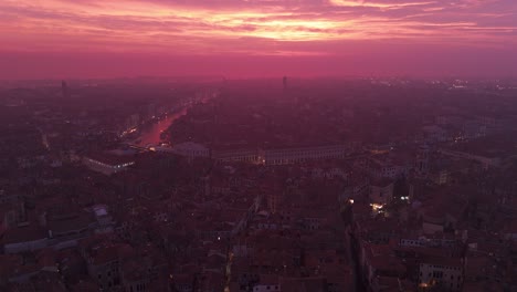 Venice-at-dusk-with-city-lights-starting-to-glow-under-a-vibrant-sunset-sky,-wide-angle,-aerial-view