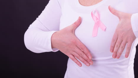 video of midsection of caucasian woman wearing pink cancer awareness ribbon, with black background