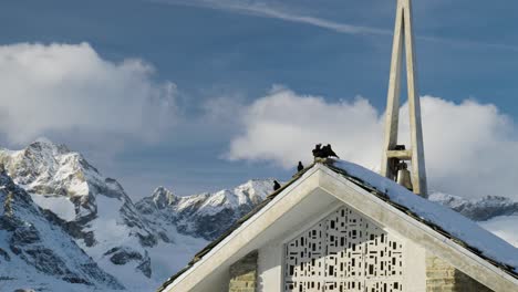 group of black birds sitting on top of small chirch covered in snow winter wonderland in zermatt glacier ski resot swiss alps