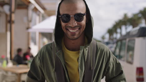 Retrato-De-Un-Hombre-Hispano-Guapo-Sonriendo-Feliz-En-La-Soleada-Playa-Con-Capucha