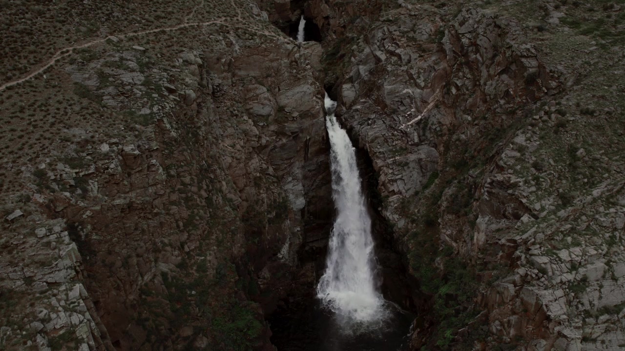 Luftfoto av Kurkure-fossen som fosser gjennom en smal steinete kløft ned i et mørkt basseng, dramatisk fjellandskap i Altai-republikken, Russland, et vilt naturlandskap