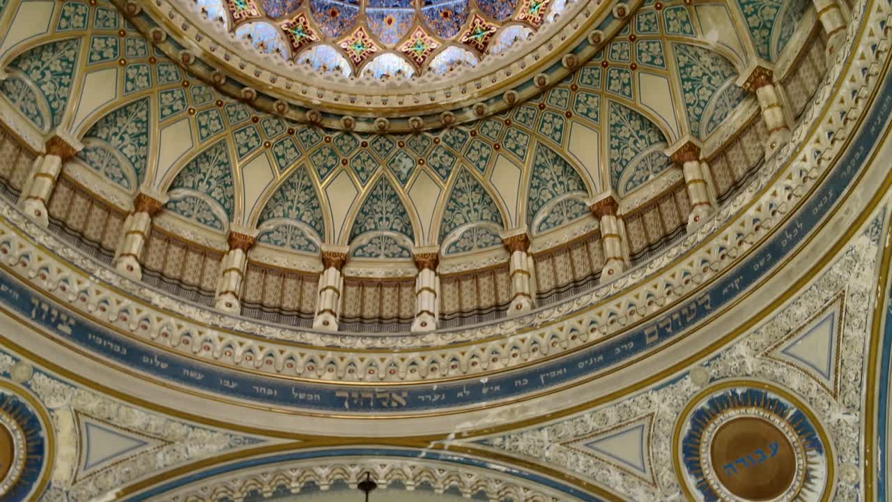 Stunning interior view of Szeged Synagogue, showing the view from the ceiling down to a window with a grand chandelier, highlighting intricate design and architectural details