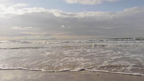 slowly backing away from gentle waves moving up and across a pristine beach on the north sea, belgium coast