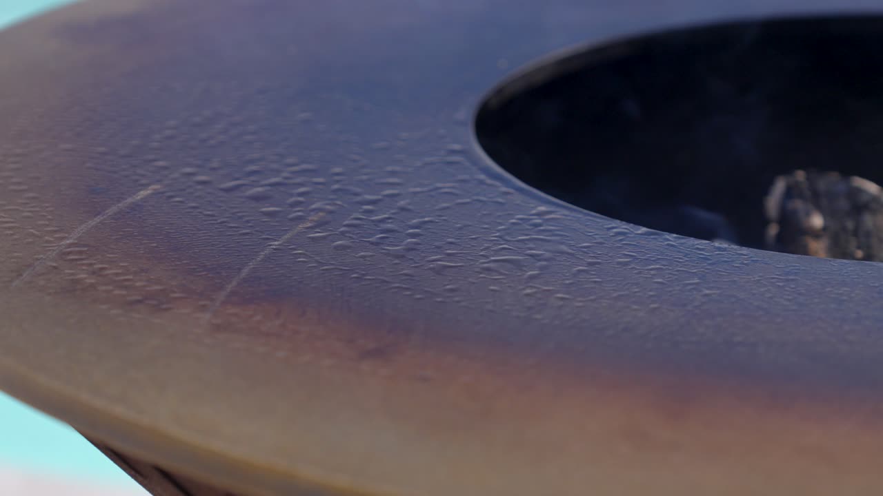 Primo piano di goccioline d'olio che si espandono su un braciere di metallo pulito