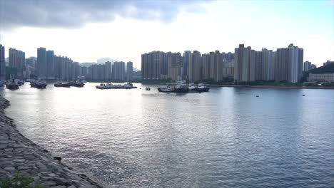 morning or evening wide view shot of barges and boats by high rise apartments in hong kong