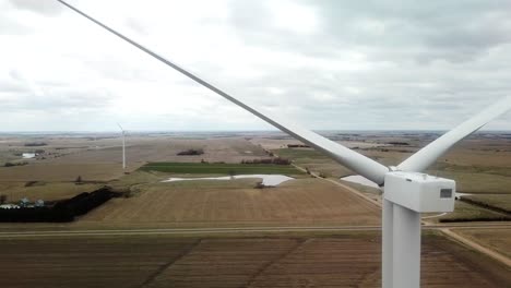 vista aérea ascendente de una turbina eólica y de las tierras agrícolas y estanques más allá de las palas de la turbina
