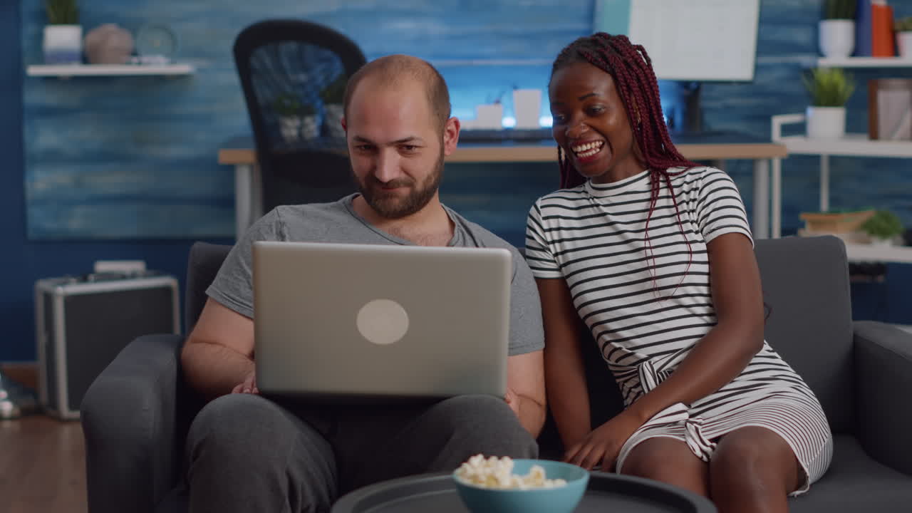 Modern interracial couple using laptop on couch at home
