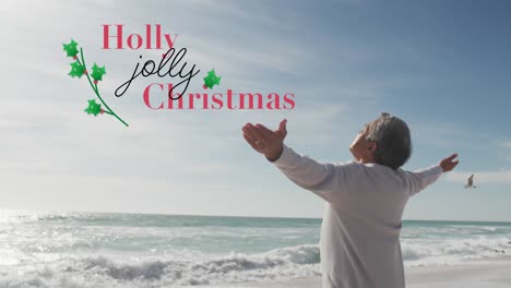 Animation-of-holly-jolly-christmas-text-over-senior-biracial-man-at-beach