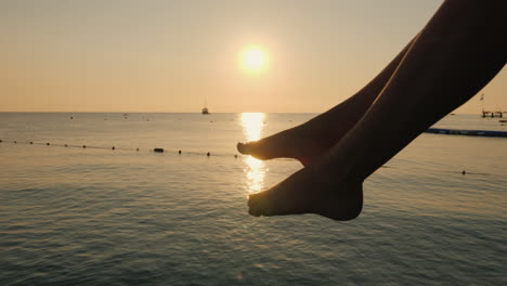 The-Woman-Carelessly-Chats-With-The-Feet-On-The-Background-Of-The-Sea-And-The-Rising-Sun-In-The-Dist