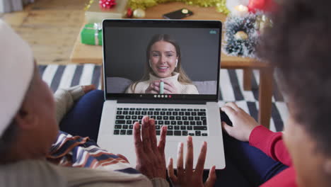 madre y hija afroamericanas usando una computadora portátil para una videollamada de navidad con una mujer en la pantalla