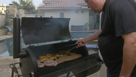 man flips bbq chicken thighs on smoking pit in backyard