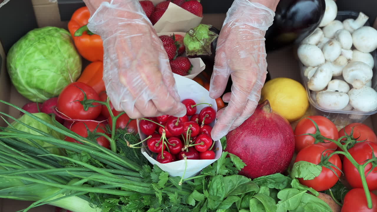 Close up of a woman's hands wearing gloves holding fresh red cherries above a box of fruits and vegetables