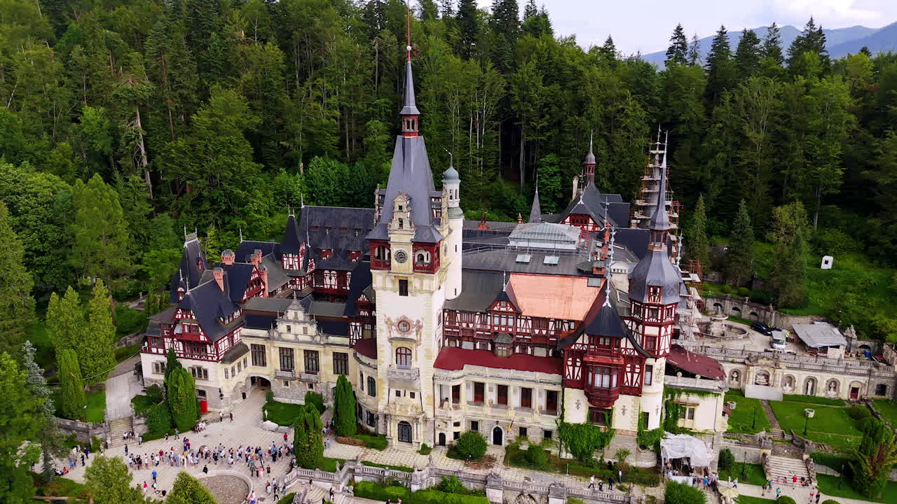 Multiple people stand in a line at the entrance to the Peles Castle in Prahova County, Romania. Aerial view on the stunning architecture at the backdrop of green forest