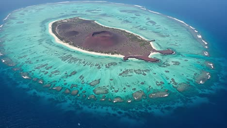 aerial view of a stunning coral atoll surrounded by vibrant turquoise waters with lush greenery on its periphery and unique geological features in the center