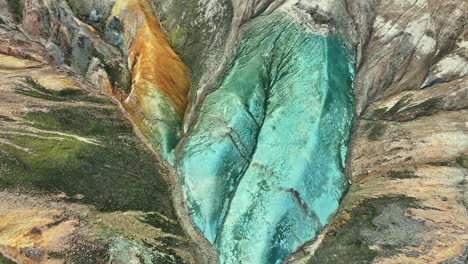 aerial drone combining rotation and bottom-to-top movement to reveal grænihryggur, the green rock in landmannalaugar, iceland, accentuating the medium tones of orange and green