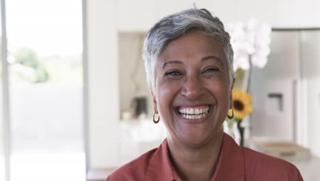 Una-Mujer-Birracial-Con-Pelo-Corto-Y-Gris-Sonríe-Cálidamente,-Vestida-Con-Una-Camisa-Roja-Y-Aretes-Dorados.