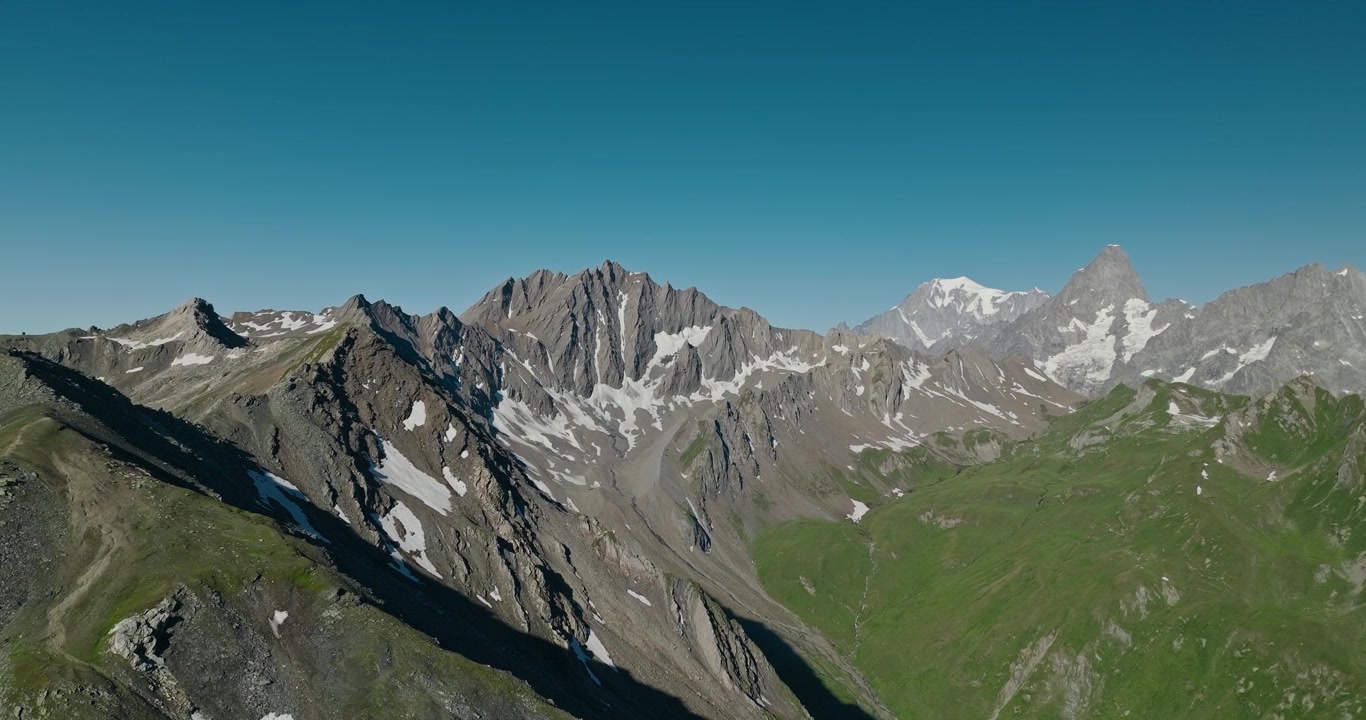 Drone terbang di atas punggung gunung yang terjal di Jalur Great St Bernard, menyingkap puncak-puncak Alpen yang spektakuler di bawah langit musim panas biru yang jernih di Pegunungan Alpen Swiss