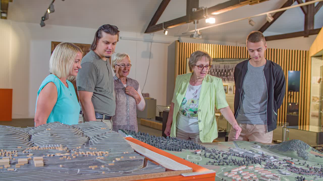 Ældre, hvid kvinde forklarer miniatureudstilling af by på Ironmaking Museum, Ravne na Koroskem, Slovenien