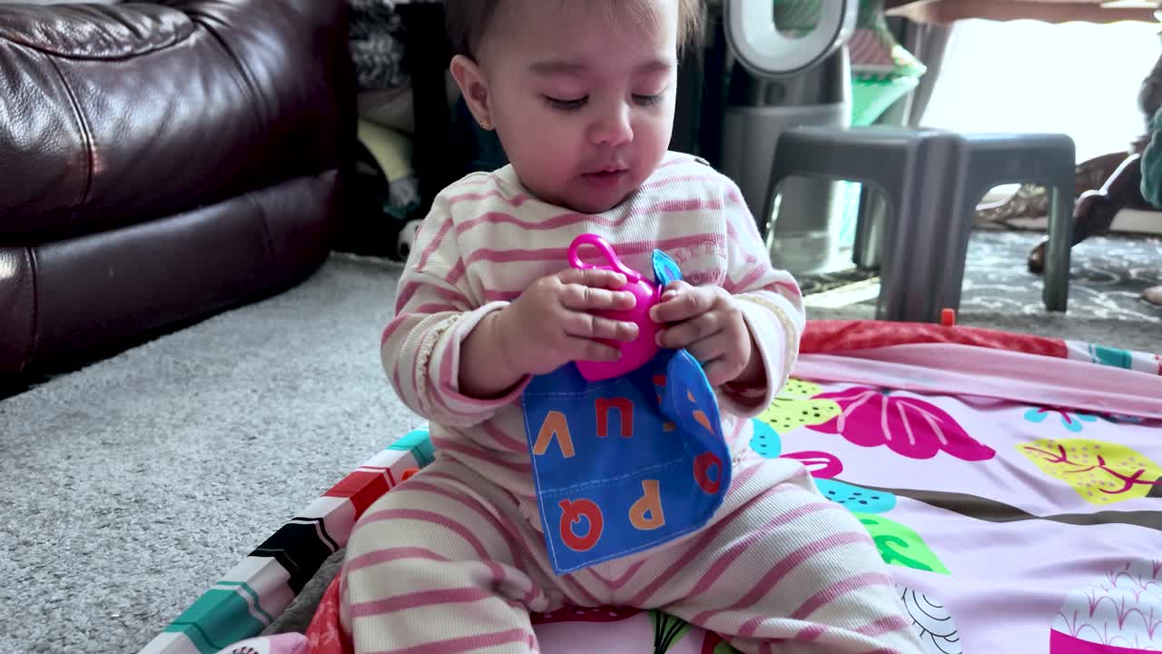 Curious South Asian baby sitting on a playmat and exploring a soft toy