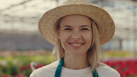 close-up portrait of a smiling woman in a straw hat and apron in a greenhouse