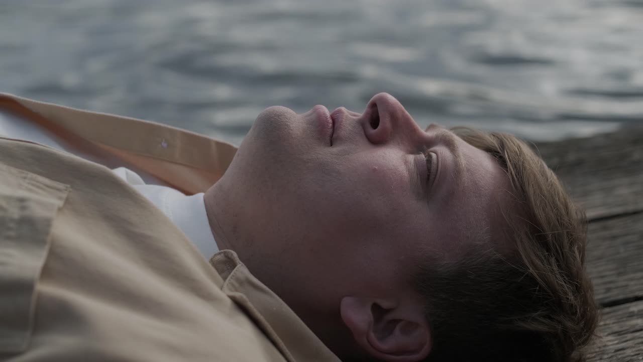 젊은이가 나무로 된 보행자 다리 위에 혼자 누워서 호수를 쳐다보고, 삶에 대해 생각하고, 자연에서 평화로운 분위기를 누리고, 신선한 공기를 즐기고, 뒤를 바라보고 있습니다.