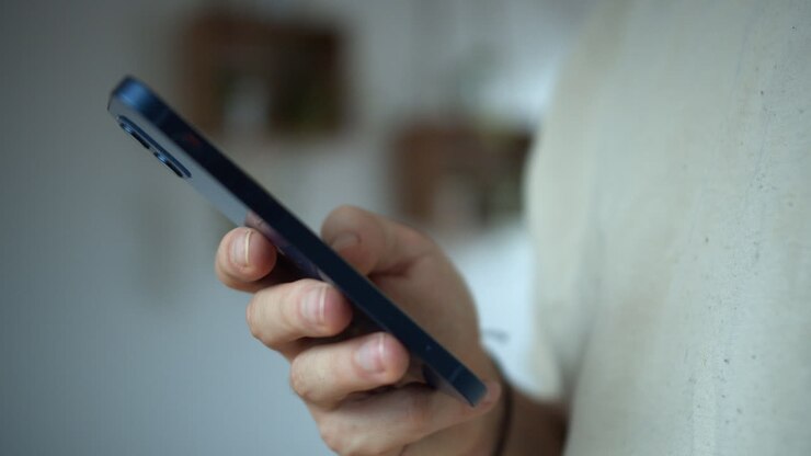 Un uomo in piedi con in mano il suo smartphone che messaggia su uno sfondo bianco isolato.
