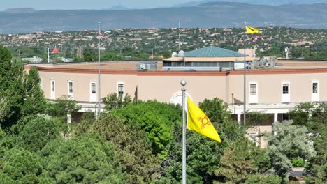 New-Mexico-state-flag-waving-in-front-of-capitol-building-in-Santa-Fe,-NM