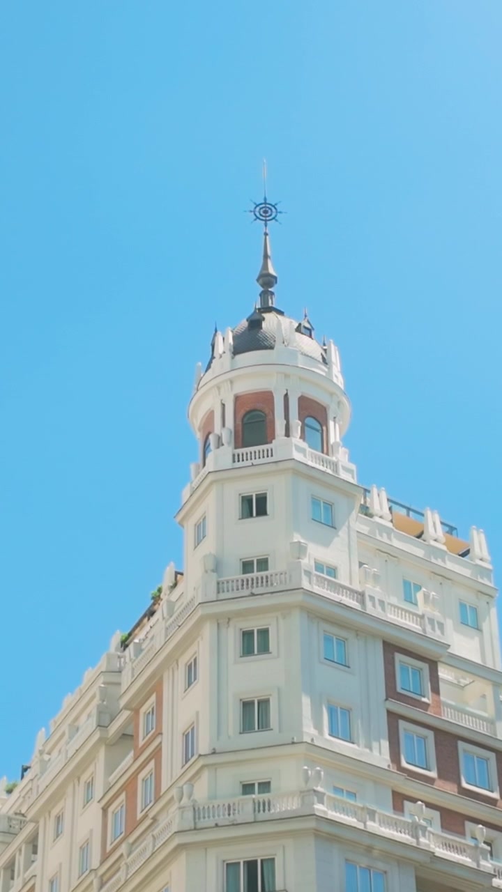 Un'inquadratura dal basso di un classico edificio bianco con una cupola decorativa e una guglia contro un cielo azzurro limpido a Madrid, Spagna. Adatto per contenuti di viaggio e cultura europea.