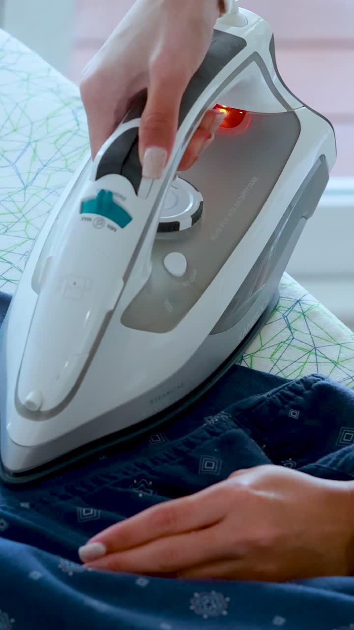 A vertical close-up shot of hands using a steam iron to press blue patterned fabric