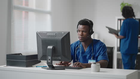 afro-american male doctor or nurse with headset and computer working at hospital .young professional therapist doctor consulting customer client using remote communication speaking on webcam