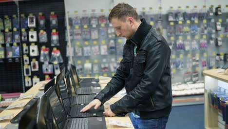 joven en el supermercado de electrónica está eligiendo una computadora portátil. variedad de computadoras portátiles en los estantes