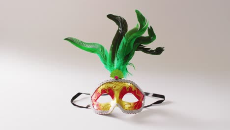 Video-of-red-and-gold-masquerade-mask-with-green-feathers-on-white-background-with-copy-space