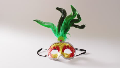 video of red and gold masquerade mask with green feathers on white background with copy space