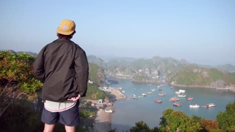 man wearing black jacket looking at the view composed of calm sea and luxury yacht in cat ba island in vietnam - aerial shot