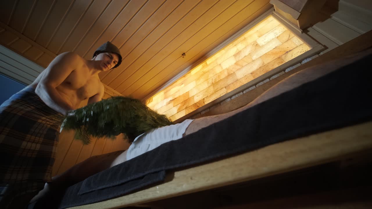 스파에서 나무 벤치에 누워있는 남자와 마사지 마사지하는 오크 자루와 함께 핀 사우나에서 실내에서 전문가와 함께 클라이언트.